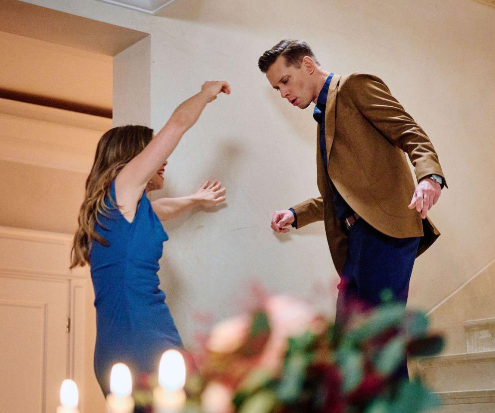 Kobieta w niebieskiej sukience spada ze schodów, podczas gdy mężczyzna w brązowej marynarce pochyla się ku niej, próbując pomóc. Scena oddaje dramatyczny moment wypadku Kaliny w dniu ślubu, o którym można przeczytać na portalu Super Seriale. W tle widać fragment schodów i dekoracji ze świecami, co podkreśla uroczysty, lecz tragiczny kontekst wydarzenia.