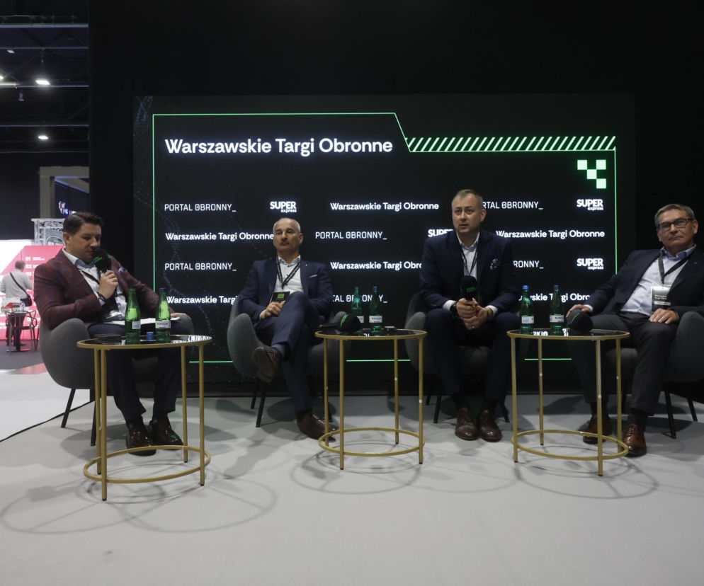 Panelist Andrzej Gruszka z mikrofonem i trzej eksperci z branży na Warszawskich Targach Obronnych, dyskutujący o łączności satelitarnej. Na czarnym ekranie logo Warszawskie Targi Obronne i Super Express. Więcej informacji o tym wydarzeniu znajdziesz na naszym portalu.