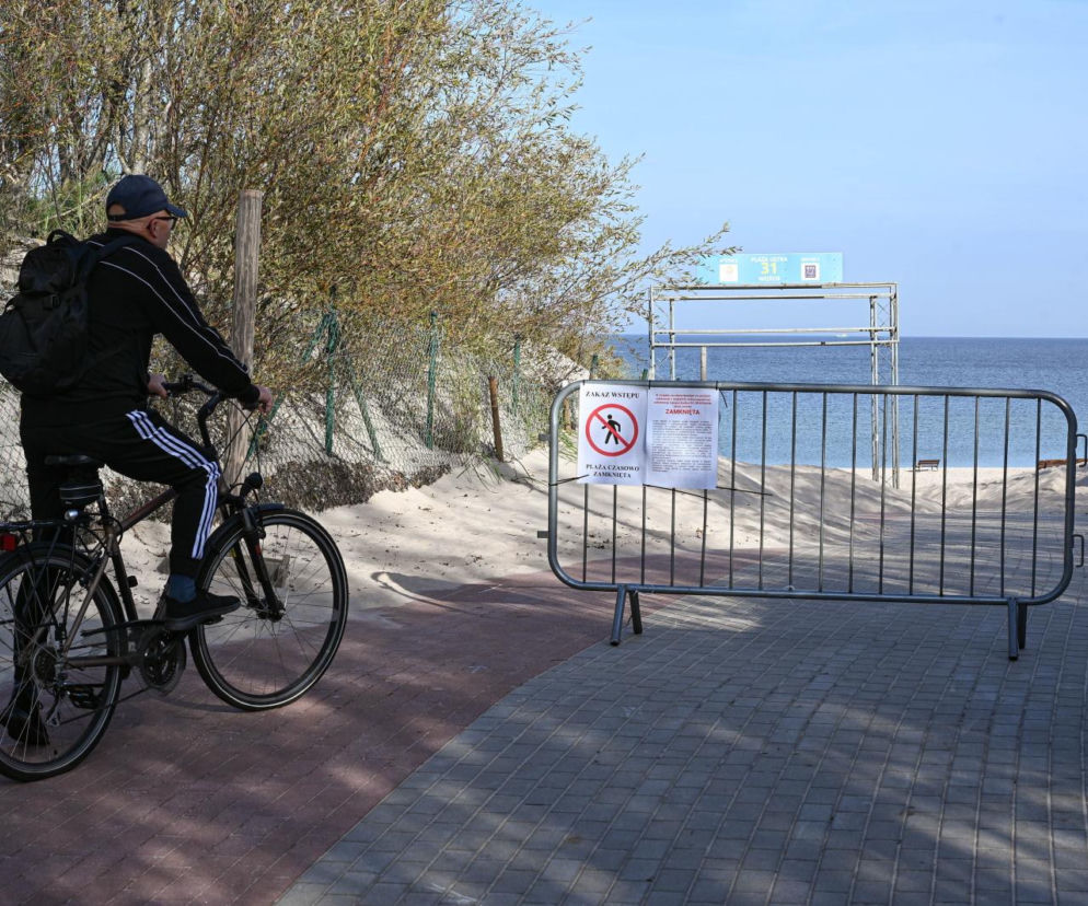Rowerzysta przed metalową barierą z zakazem wstępu na plażę w Ustce. O skażeniu Bałtyku przeczytasz na SE.