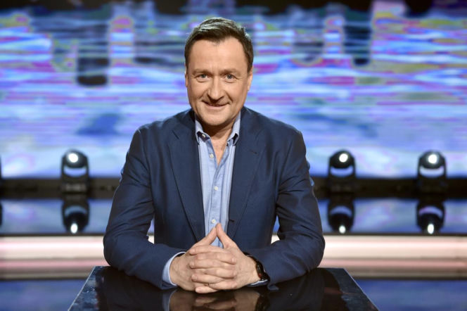 Uśmiechnięty Jacek Kawalec w niebieskiej marynarce siedzi przy stole. O odejściu artysty z Budki Suflera czytaj na EskaRock.