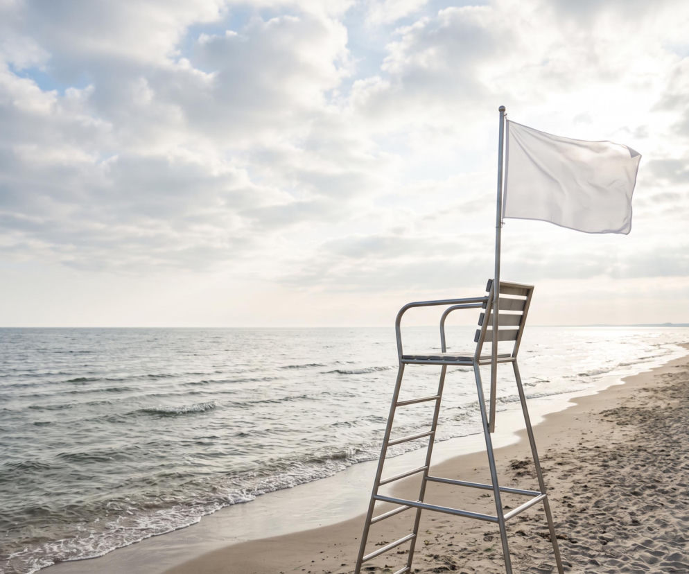 Biała flaga na wieży ratowniczej przy pustej plaży. O bezpiecznej kąpieli w Trzęsaczu przeczytasz na SE Szczecin.