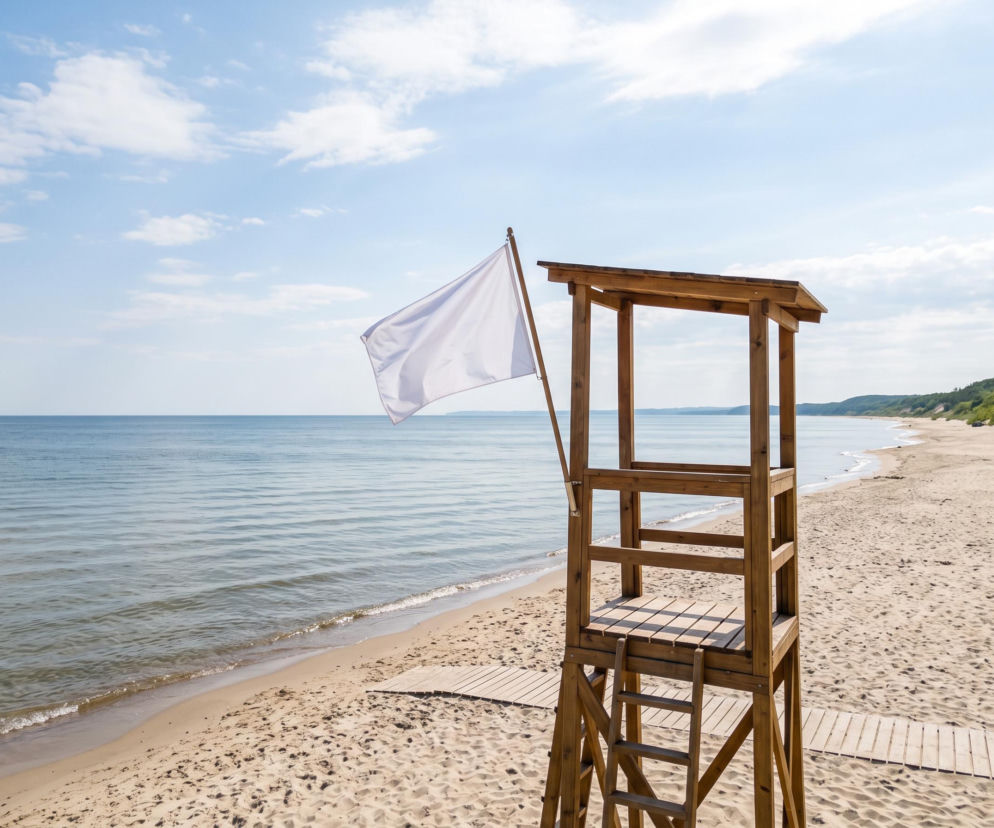Drewniana wieża ratownicza z białą flagą na pustej plaży w Grzybowie. O warunkach nad morzem przeczytasz w SE Szczecin.