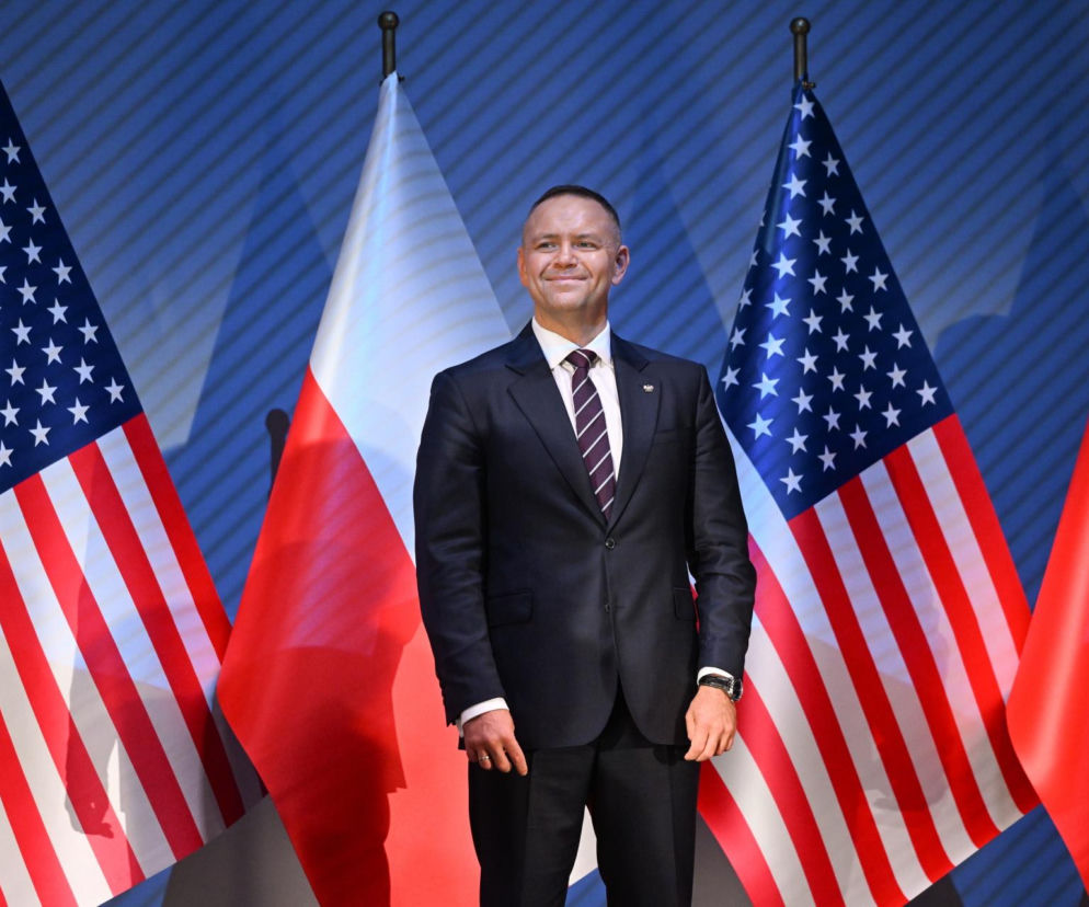 Uśmiechnięty Karol Nawrocki w ciemnym garniturze na tle flag Polski i USA. O kulisach gali w Waszyngtonie przeczytasz w Eska.