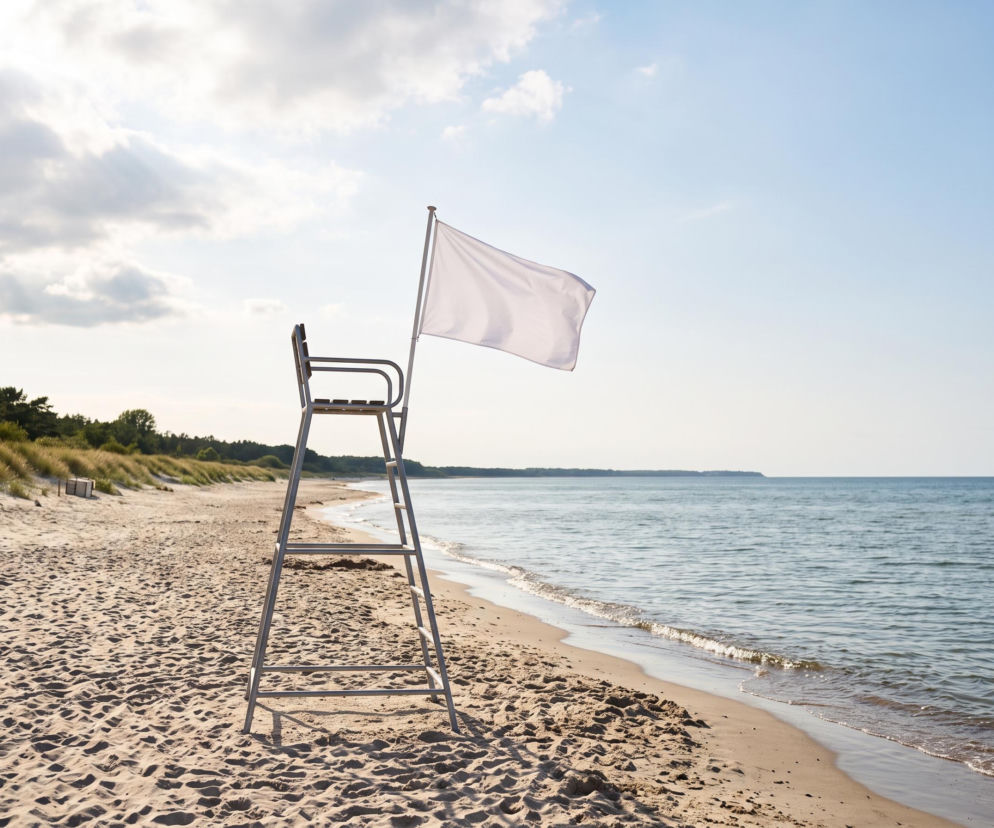 Biała flaga na wieży ratowniczej na pustej plaży w Dąbkach. O warunkach nad Bałtykiem przeczytasz na SE Szczecin.