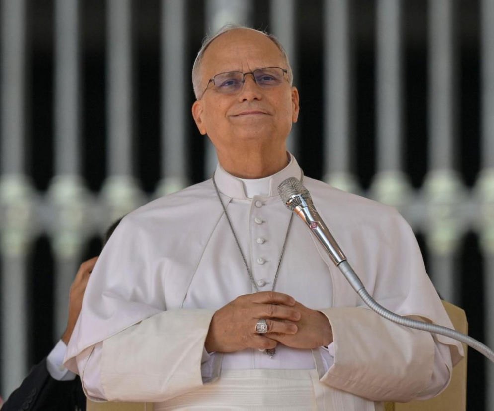 Uśmiechnięty papież Leon XIV stoi przed mikrofonem. O dobrym stanie zdrowia Ojca Świętego przeczytasz na SE.