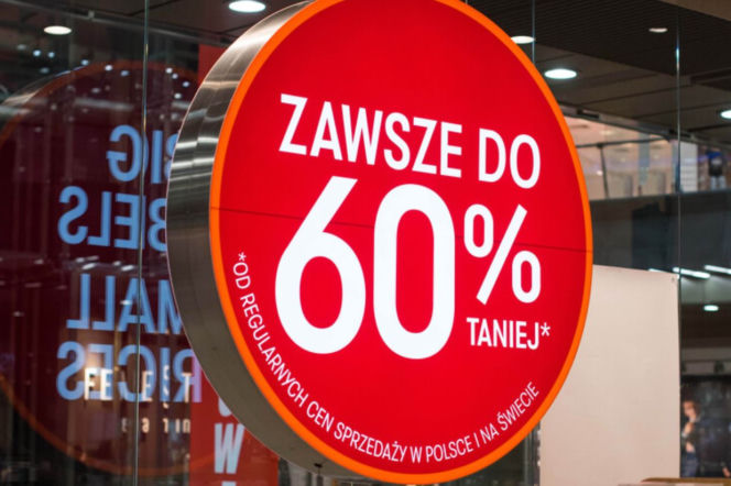 Czerwony szyld reklamowy z napisem „Zawsze do 60% taniej”. O markowych prezentach w TK Maxx przeczytasz na SE.