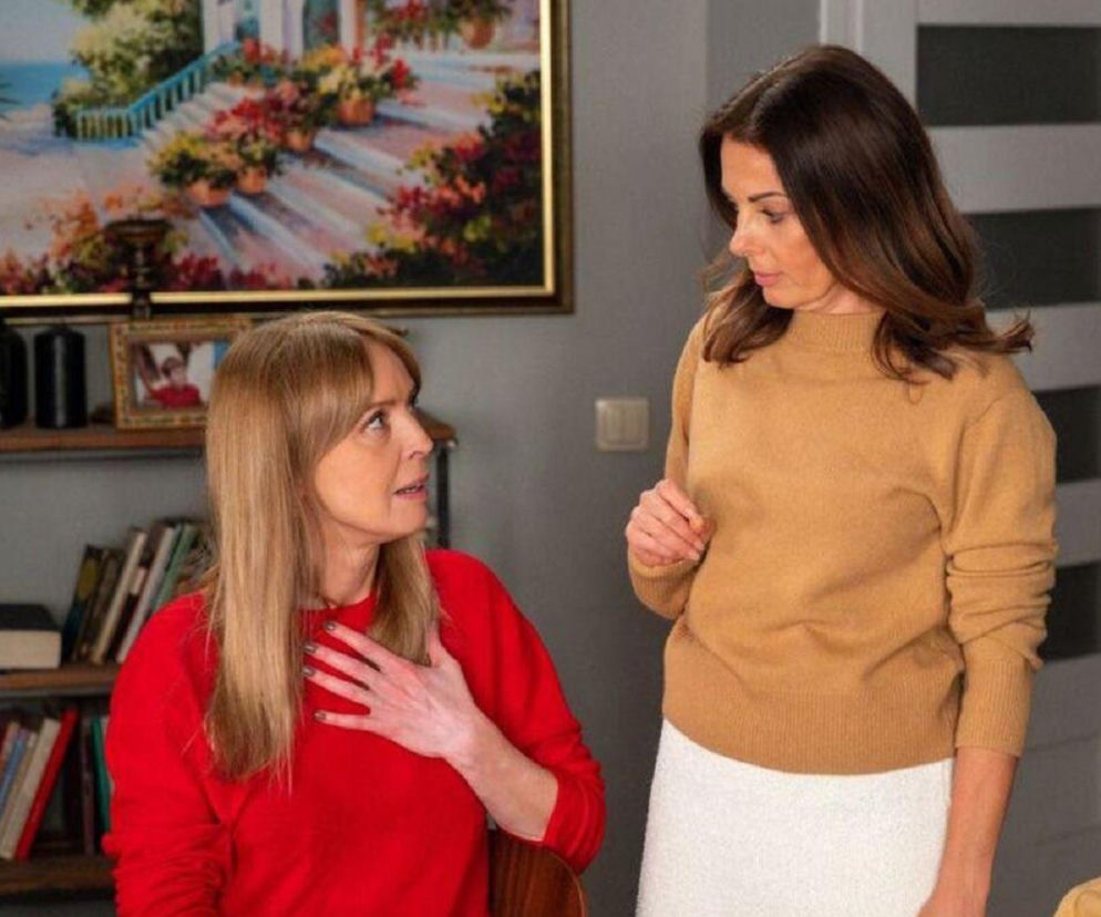 Agnieszka (Katarzyna Tlałka) w czerwonym swetrze, z dłonią na klatce piersiowej, rozmawia z Kasią (Katarzyna Glinka) w brązowym swetrze i białej spódnicy. Kobiety intensywnie dyskutują, ich mimika wskazuje na poważną rozmowę o problemach w serialu Barwy szczęścia. Więcej o tym na stronie Super Seriale.