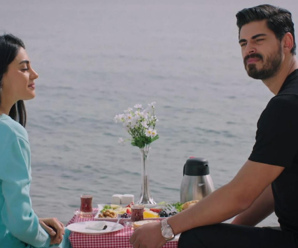 Hancer i Cihan podczas romantycznego śniadania na plaży, siedzą przy stole z białym obrusem w czerwoną kratę, oboje ubrani są w jasne i ciemne ubrania. Cihan wyznaje żonie swoje oczekiwania po pierwszej wspólnej nocy w 76. odcinku telenoweli „Panna młoda” na Super Seriale.