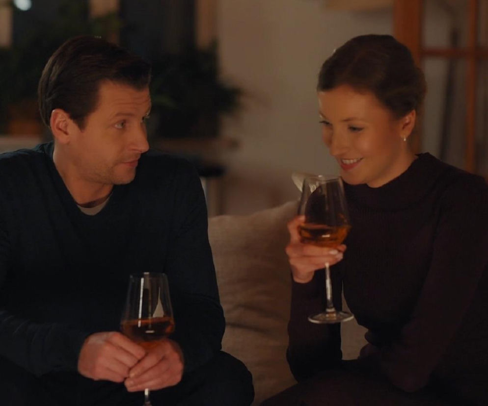 Uśmiechnięta Natalka Mostowiak (Dominika Suchecka) i Adam Karski (Patryk Szwichtenberg) siedzą razem na kanapie, trzymając kieliszki z winem. Para rozmawia, Natalka spogląda na Adama z zadowoleniem. Więcej o ich losach na Super Seriale.