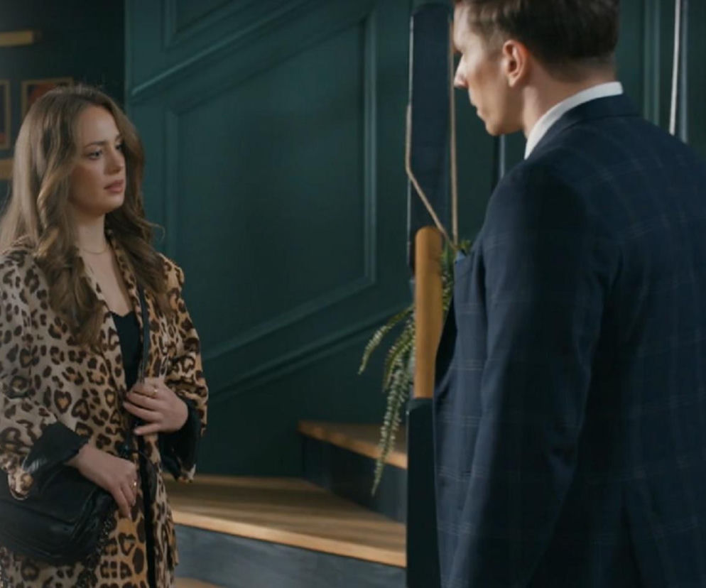 Oliwka (Wiktoria Gąsiewska) w eleganckim płaszczu w panterkę i z czarną torebką rozmawia z Tomkiem (Jakub Sokołowski) w garniturze. Scena z serialu Barwy szczęścia w hotelu Stańskich, gdzie bohaterka zamieszkała. Więcej informacji o serialu Barwy szczęścia na Super Seriale.
