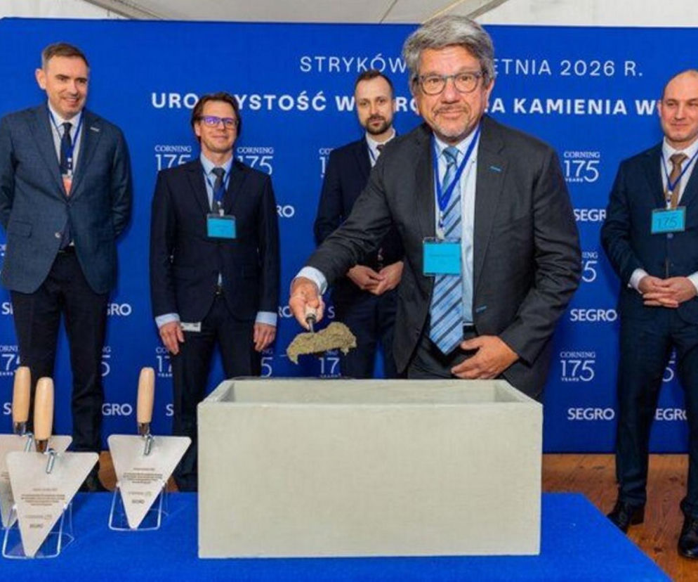 Uroczystość wmurowania kamienia węgielnego pod fabrykę Corning Incorporated w Strykowie. Mężczyzna w okularach sypie beton do skrzyni, obok stoją inni uczestnicy. Więcej o inwestycji przeczytasz na Super Biznes.