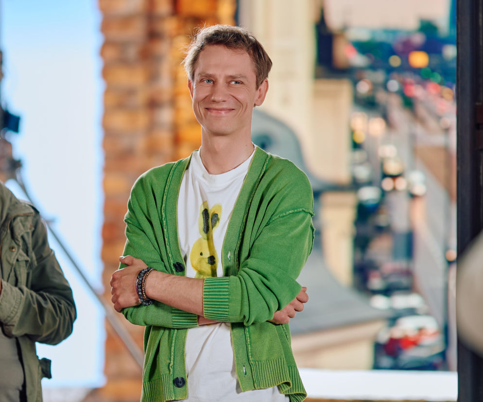 Uśmiechnięty Fabian Krawiec w zielonym kardiganie na planie programu. O serialu Na Wspólnej przeczytasz na SE Superseriale.