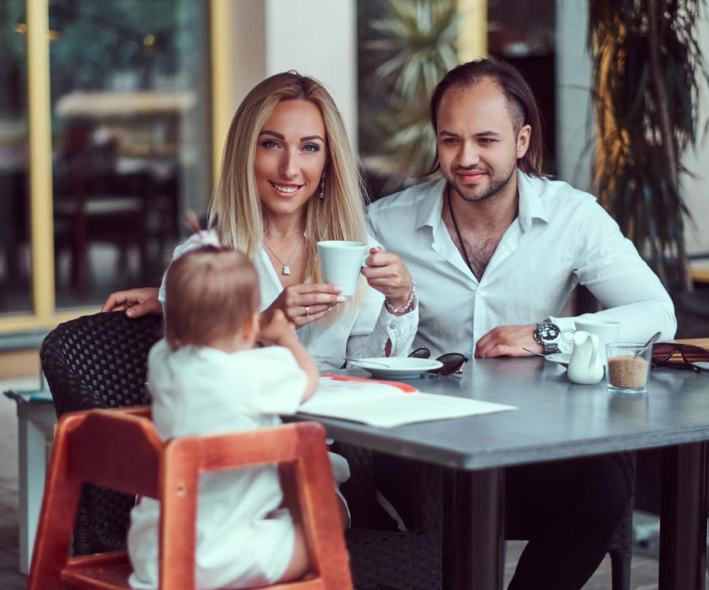 Uśmiechnięci rodzice z małym dzieckiem w restauracji. Porady dla rodziców na temat wyjść z dziećmi znajdziesz na SE.
