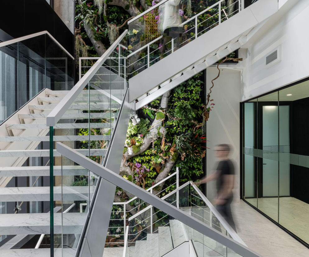 Nowoczesna, wielopiętrowa klatka schodowa z białymi, marmurowymi stopniami i szklanymi balustradami w biurze kancelarii CMS Polska w Varso Tower, zaprojektowana przez Trzop Architekci. Obok schodów znajduje się bujny, zielony ogród wertykalny. Więcej o tym na Architektura Murator Plus.