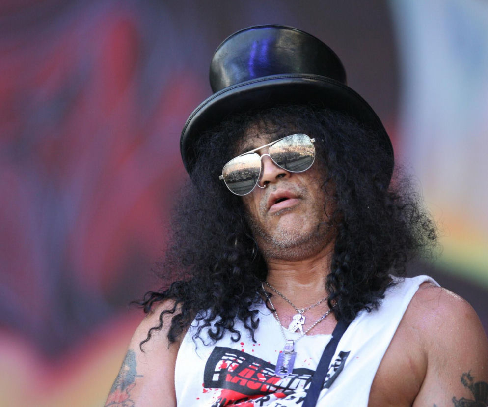 Portret Slasha, legendarnego gitarzysty Guns N' Roses, w czarnym cylindrze i okularach lustrzankach, z burzą kręconych włosów. Na szyi widoczne są charakterystyczne naszyjniki. Możesz przeczytać więcej o karierze Slasha na naszym portalu.