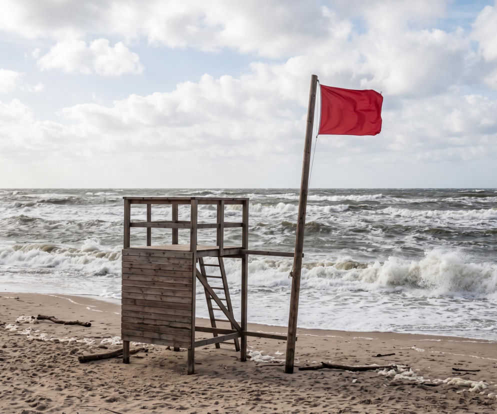 Czerwona flaga na pustej plaży w Łazach przy wzburzonym morzu. O zakazie kąpieli przeczytasz na SE Szczecin.