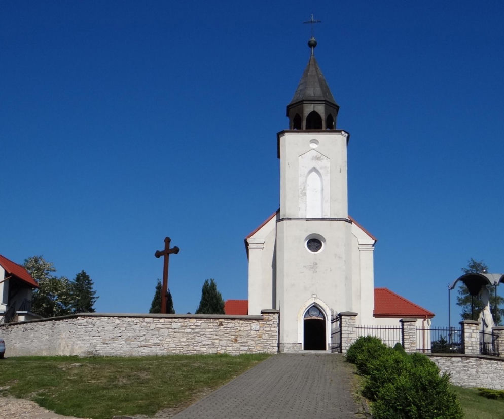 Biały kościół z wysoką wieżą we wsi Bydlin na tle błękitnego nieba. O historii regionu przeczytasz w Eska Kraków.