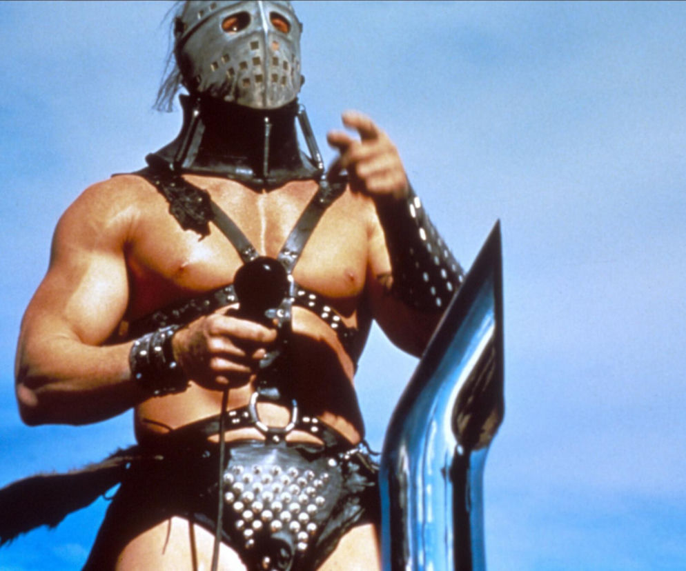 Kjell Nilsson jako Lord Humungus w filmie Mad Max 2 na tle błękitnego nieba. O śmierci aktora przeczytasz w Eska.