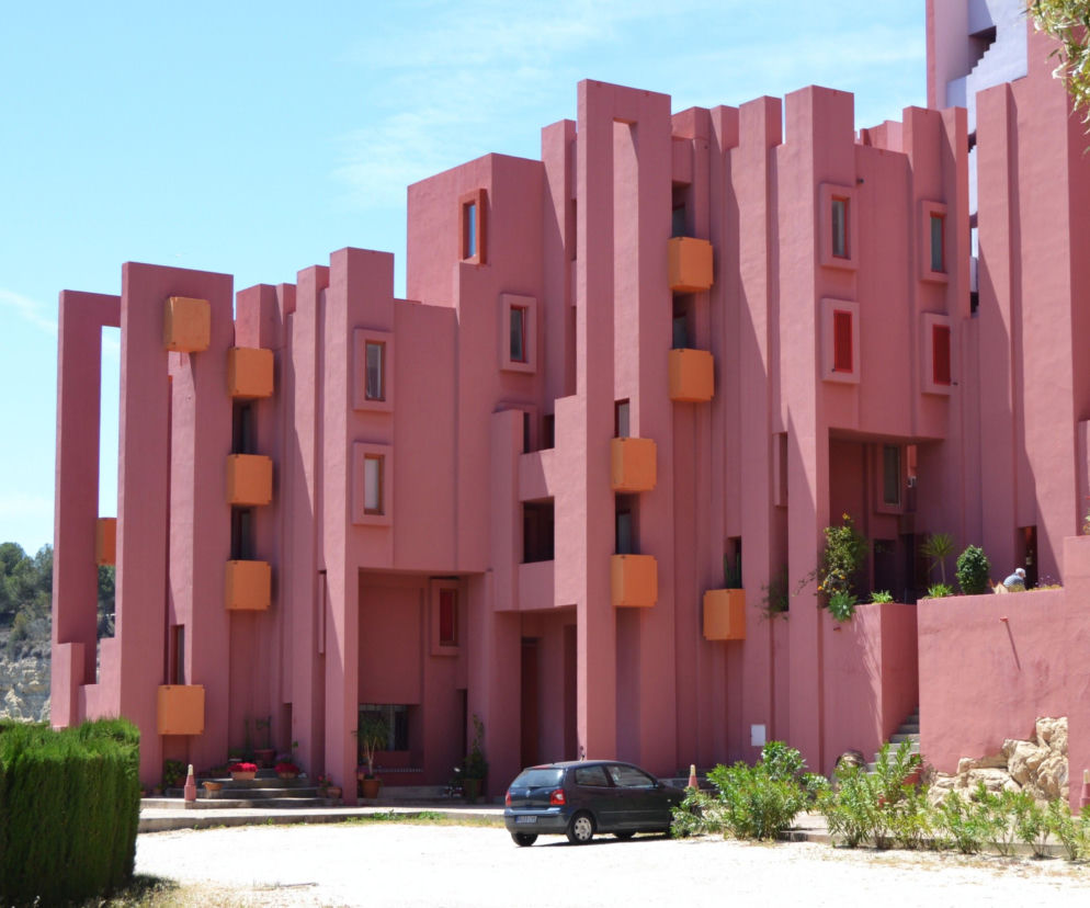 Muralla Roja w Calpe, Hiszpania, to architektoniczne arcydzieło Ricardo Bofilla, przypominające fortyfikacje. Czerwone ściany budynku z pomarańczowymi elementami i wąskimi oknami tworzą efektowny kontrast z jasnym, błękitnym niebem. Więcej o tym projekcie na Architektura Murator Plus.