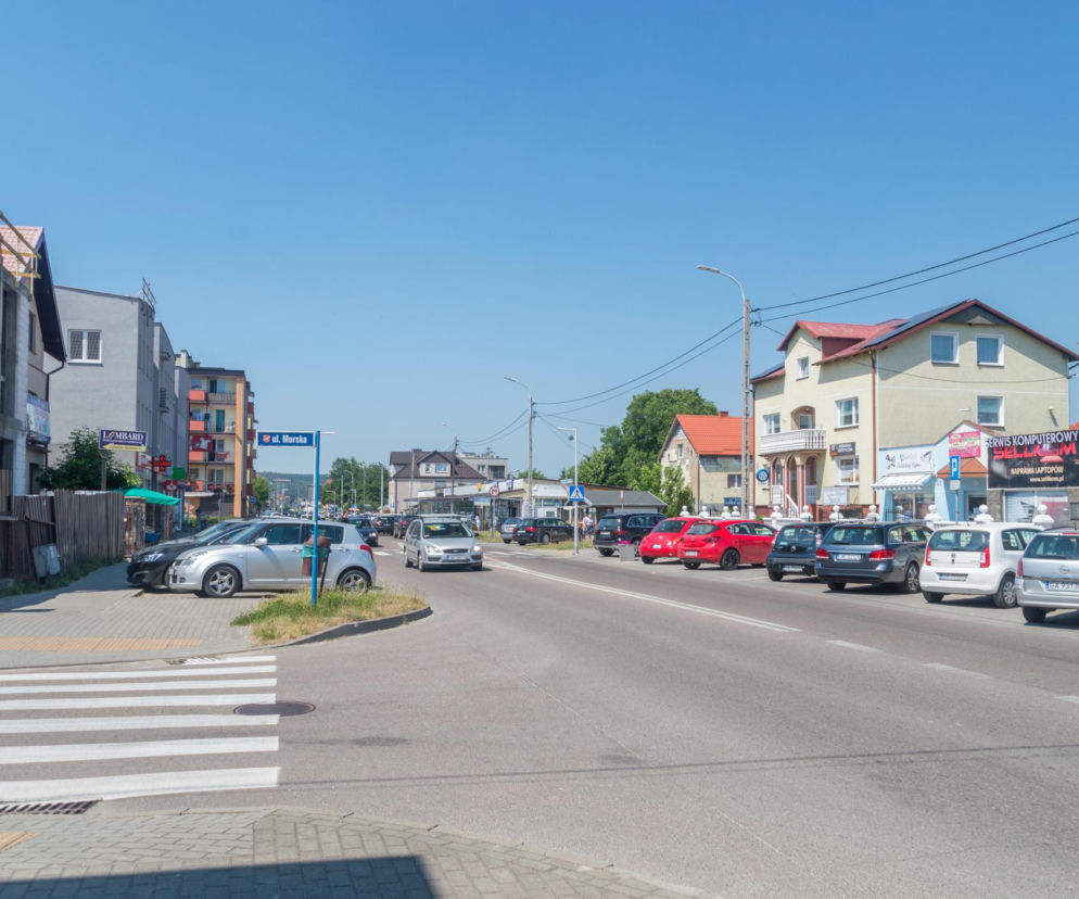 Ulica Morska w Rumi z widoczną zabudową mieszkalno-usługową oraz zaparkowanymi samochodami, symbolizująca rozwój aglomeracji trójmiejskiej. Informacje o inwestycjach deweloperskich w Rumi i ich wpływie na rynek nieruchomości znajdziesz na naszym portalu.