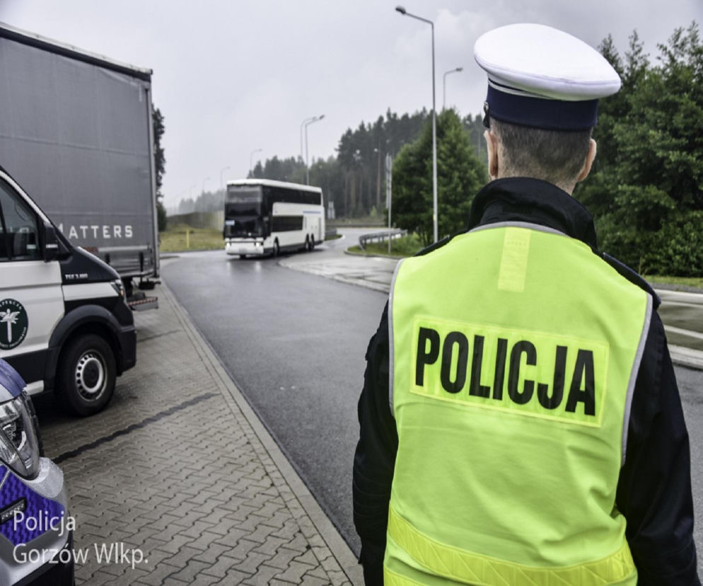 Policjant w odblaskowej kamizelce obserwuje drogę i jadący autokar. O akcji bezpieczny powrót czytaj na Eska Siedlce.