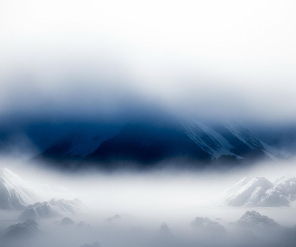 Dominujący jest tu górski krajobraz zimowy, spowity gęstą mgłą i chmurami. W centralnej części obrazu widoczna jest ciemna, granatowa góra, częściowo pokryta śniegiem i lodem, wystająca zza warstwy niebieskawej mgły. Na pierwszym planie, u dołu, rozciąga się pasmo ośnieżonych, skalistych szczytów i dolin, zanurzonych w gęstej, białej mgle. Górna część obrazu to jasne, niemal białe niebo, przechodzące w błękitną poświatę chmur okalających szczyty.