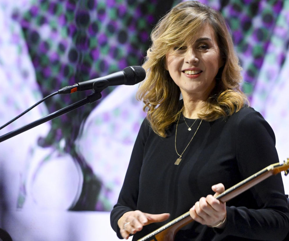 Edyta Bartosiewicz uśmiecha się podczas występu z gitarą. O roli jurorki w The Voice of Poland przeczytasz w Eska.