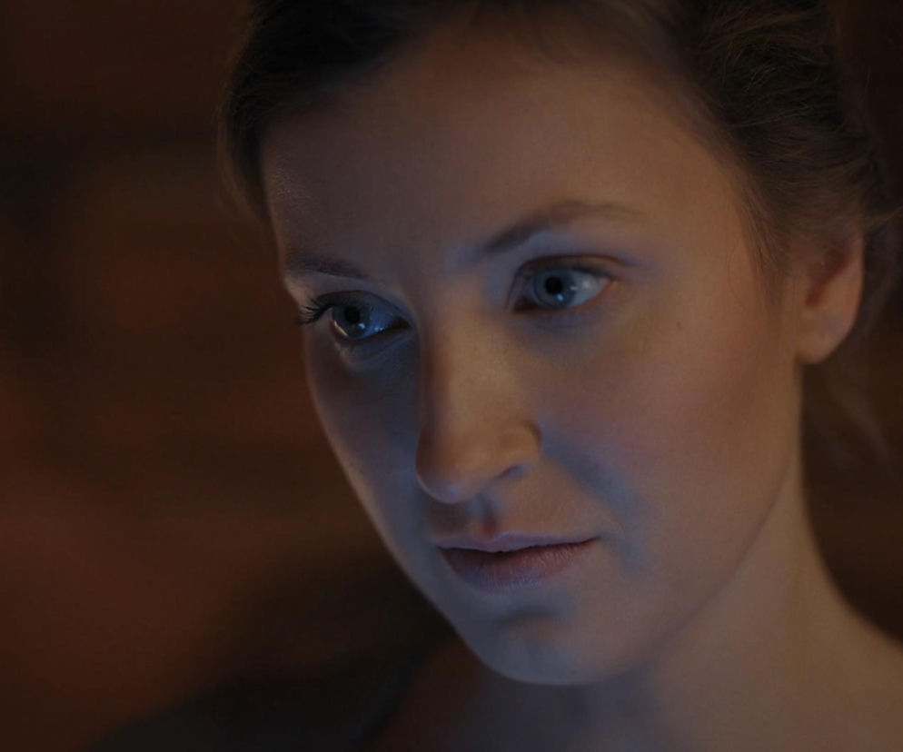 Zbliżenie na twarz Natalki (Dominika Suchecka) z serialu M jak miłość, pogrążonej w zamyśleniu, z delikatnym niebieskim światłem odbijającym się w jej oczach, symbolizującym jej dylematy uczuciowe. Więcej o losach bohaterki przeczytasz na Super Seriale.