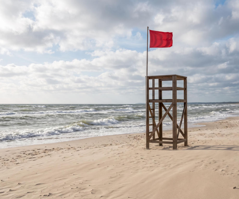 Drewniana wieża ratownicza z czerwoną flagą na plaży w Dąbkach. O zakazie kąpieli przeczytasz na SE Szczecin.