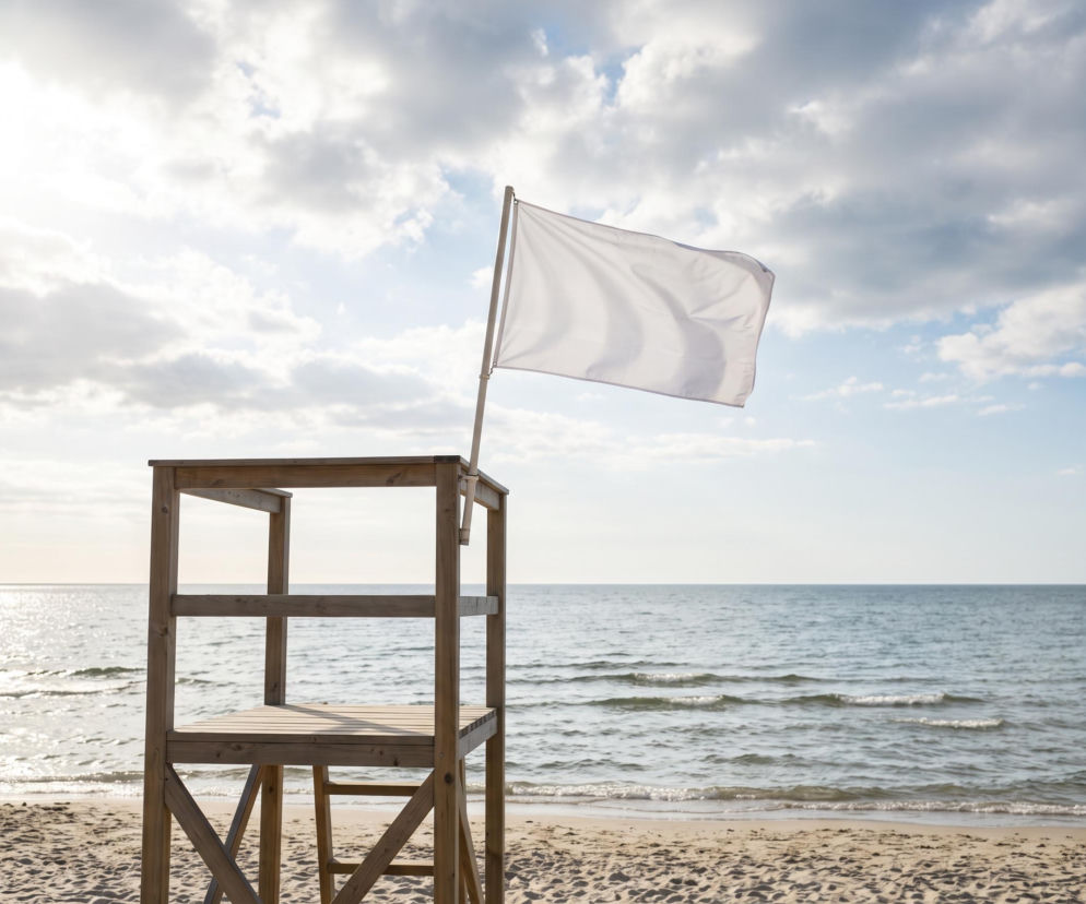 Drewniana wieża ratownicza z białą flagą na plaży w Grzybowie. O bezpieczeństwie nad wodą przeczytasz na SE Szczecin.