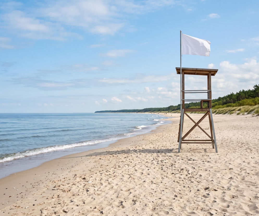 Biała flaga na wieży ratowniczej przy pustej plaży w Mielnie. O bezpieczeństwie kąpieli przeczytasz na SE Szczecin.