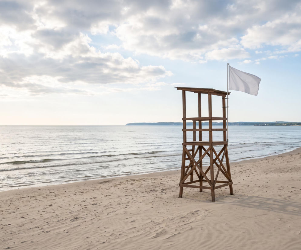 Drewniana wieża ratownicza na plaży w Świnoujściu z białą flagą. O bezpieczeństwie kąpieli przeczytasz na SE Szczecin.