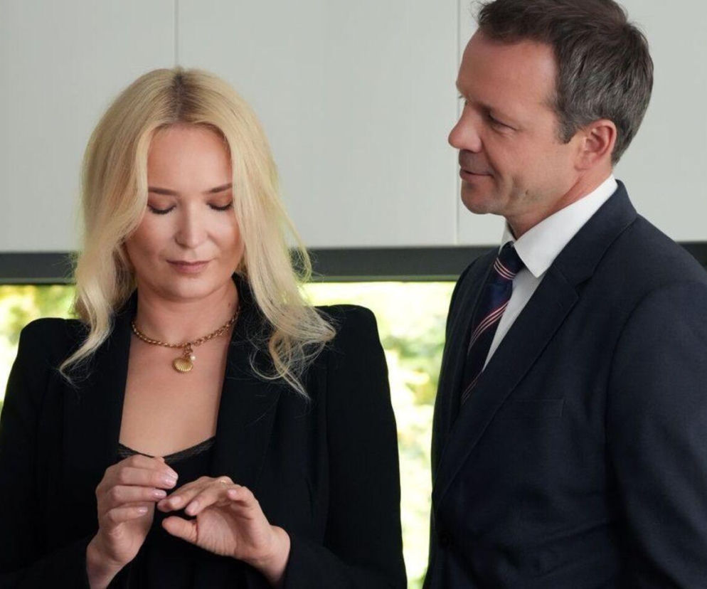 Karolina i Bruno z Barw szczęścia w nowym sezonie. Kobieta ma na sobie czarną marynarkę i naszyjnik, patrząc w dół. Mężczyzna w garniturze spogląda na nią. Konflikt o intercyzę to główny wątek, o którym przeczytasz na Super Seriale.