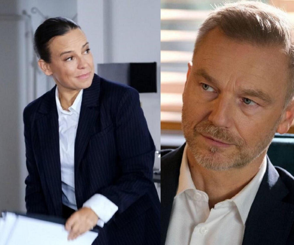 Na zdjęciu Anna Prus jako Anna Sadowska i Krystian Wieczorek w roli Andrzeja Budzyńskiego z serialu M jak miłość. Sadowska, ubrana w granatowy garnitur i białą koszulę, patrzy w prawo, a Budzyński, w białej koszuli i marynarce, patrzy w lewo. Dowiedz się więcej o Super Seriale.