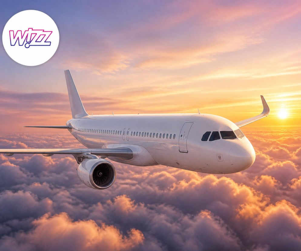 Biały samolot pasażerski leci nad chmurami o zachodzie słońca. Obok logo Wizz Air. O promocji linii przeczytasz na SE.