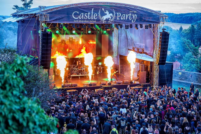 Zespół muzyczny z wokalistą grający na scenie festiwalu Castle Party z efektami ognia i rzeszą fanów pod sceną. Zdjęcie ilustruje, jak błędy na festiwalu mogą zrujnować zdrowie, o czym przeczytasz na Poradnik Zdrowie.