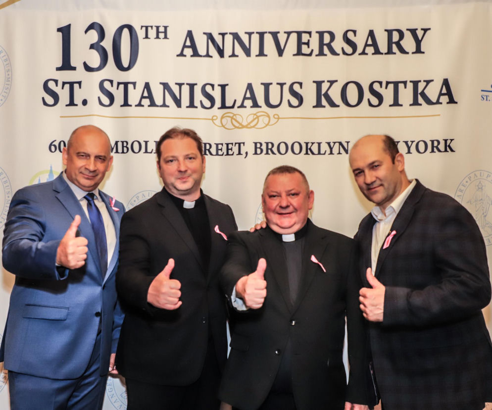 Czterech uśmiechniętych mężczyzn na tle banneru 130-lecia parafii św. Stanisława Kostki. O jubileuszu pisze SE USA.