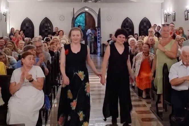 Dwie artystki w czarnych sukniach idą przez kościół wypełniony ludźmi. O festiwalu w Lublinie przeczytasz na Radioplus.