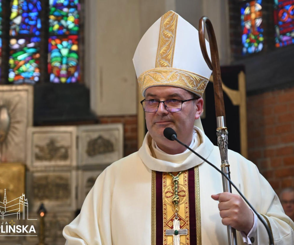 Biskup Przemysław Szulc podczas Eucharystii prymicyjnej w bazylice w Chojnicach, ubrany w białą mitrę ze złotymi zdobieniami oraz albę i ornat, trzymający pastorał. W tle widoczne witraże i ceglana ściana. Więcej o tym wydarzeniu przeczytasz na naszym portalu.