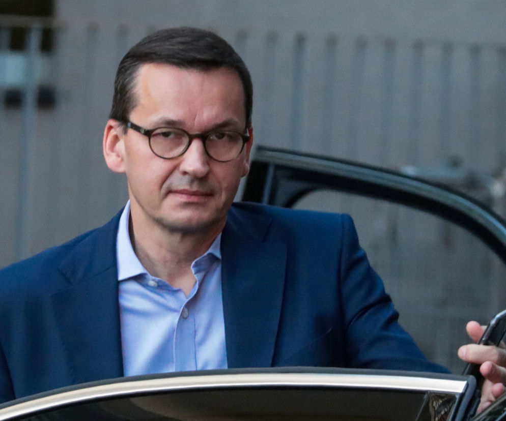Były premier Mateusz Morawiecki wysiada z samochodu, trzymając smartfon. O jego pomyśle na migrantów czytaj na SE Polityka.