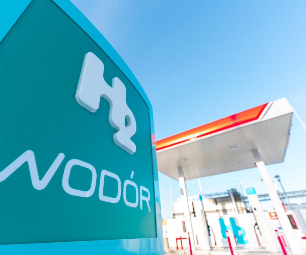 Zielony szyld WODÓR z symbolem H2 na tle niebieskiego nieba, obok widoczna nowoczesna stacja paliw ORLEN w Pile. Inwestycja wspiera niskoemisyjny transport. Więcej o stacji wodorowej w Pile przeczytasz na Super Biznes.