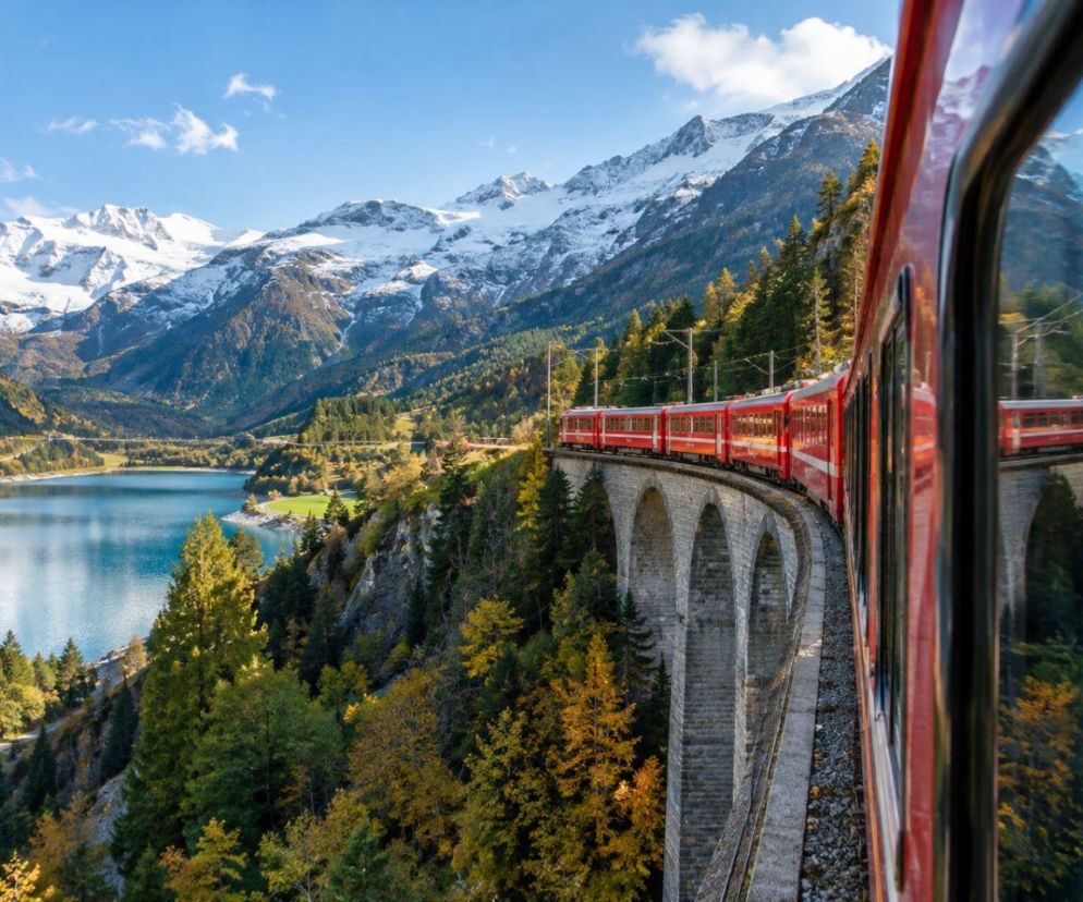 Czerwony pociąg Bernina Express jadący przez wysoki, kamienny wiadukt w Alpach. O podróży marzeń przeczytasz na SE.