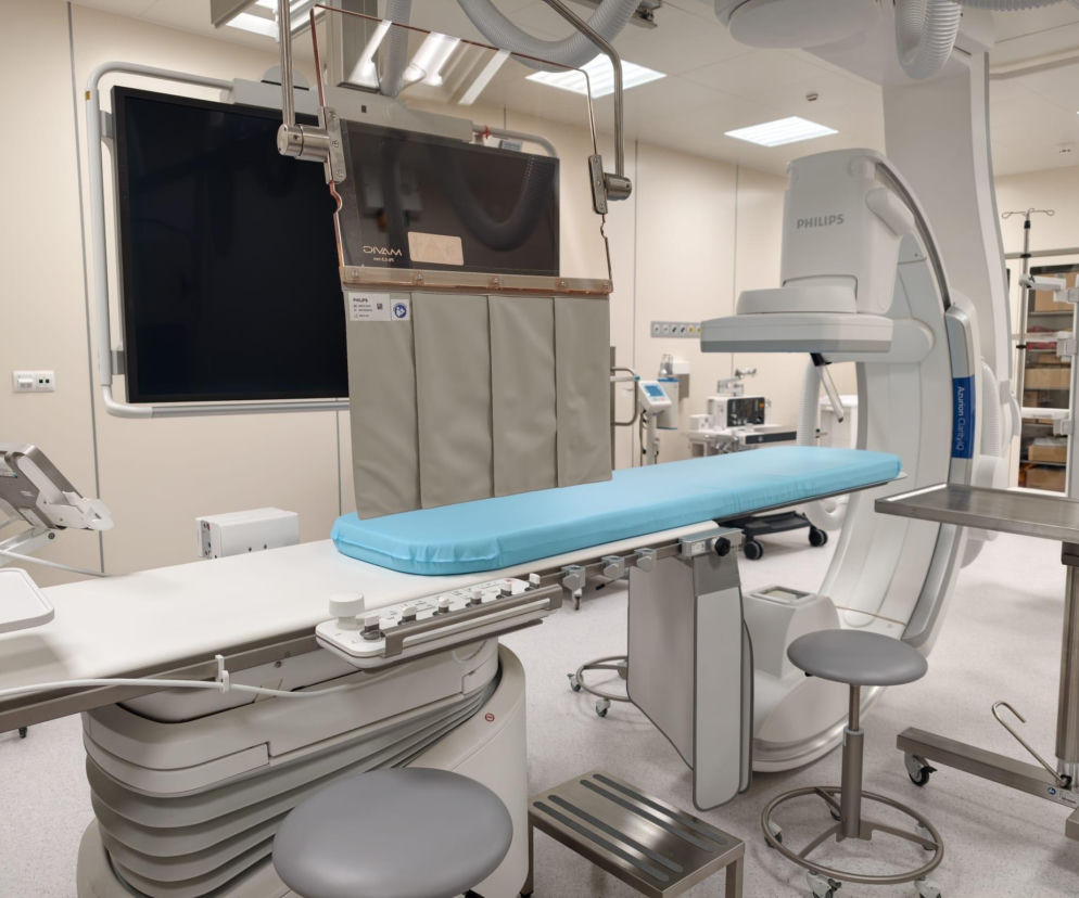 Nowocześnie wyposażona sala zabiegowa w Szpitalu Uniwersyteckim w Zielonej Górze. Widoczne łóżko zabiegowe z niebieskim materacem, aparatura medyczna Philips do elektrofizjologii serca, monitory i lampy. O modernizacji kardiologii przeczytasz na naszym portalu.