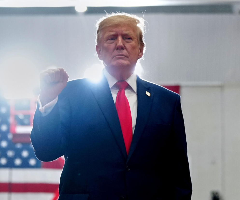 Donald Trump z uniesioną pięścią na tle flagi USA. O propozycji zmiany nazwy AI na SI przeczytasz na SE.