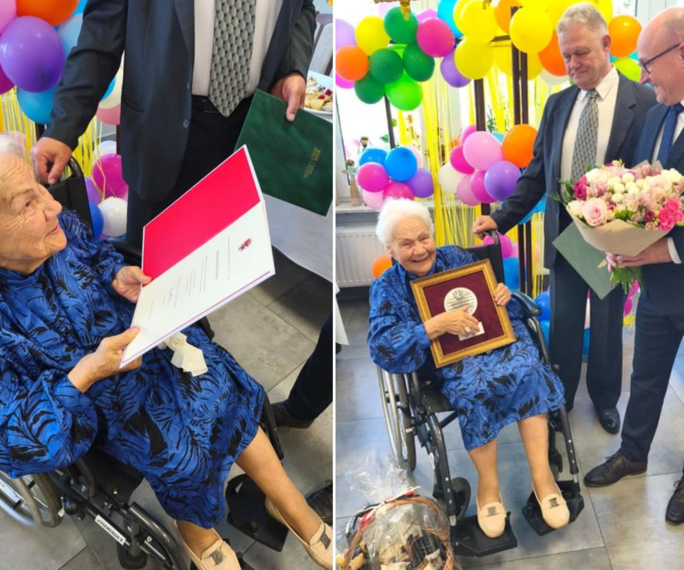 Uśmiechnięta pani Bernardyna Fischer w niebieskiej sukience, siedząca na wózku inwalidzkim, odbiera medal i bukiet kwiatów od mężczyzn podczas obchodów swoich 100. urodzin. Więcej o jej niezwykłym życiu przeczytasz na naszym portalu.