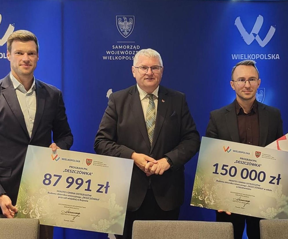 Trzej mężczyźni z tablicami symbolizującymi czeki na deszczówkę. O dotacjach dla Ostrzeszowa pisze Eska Ostrzeszów.