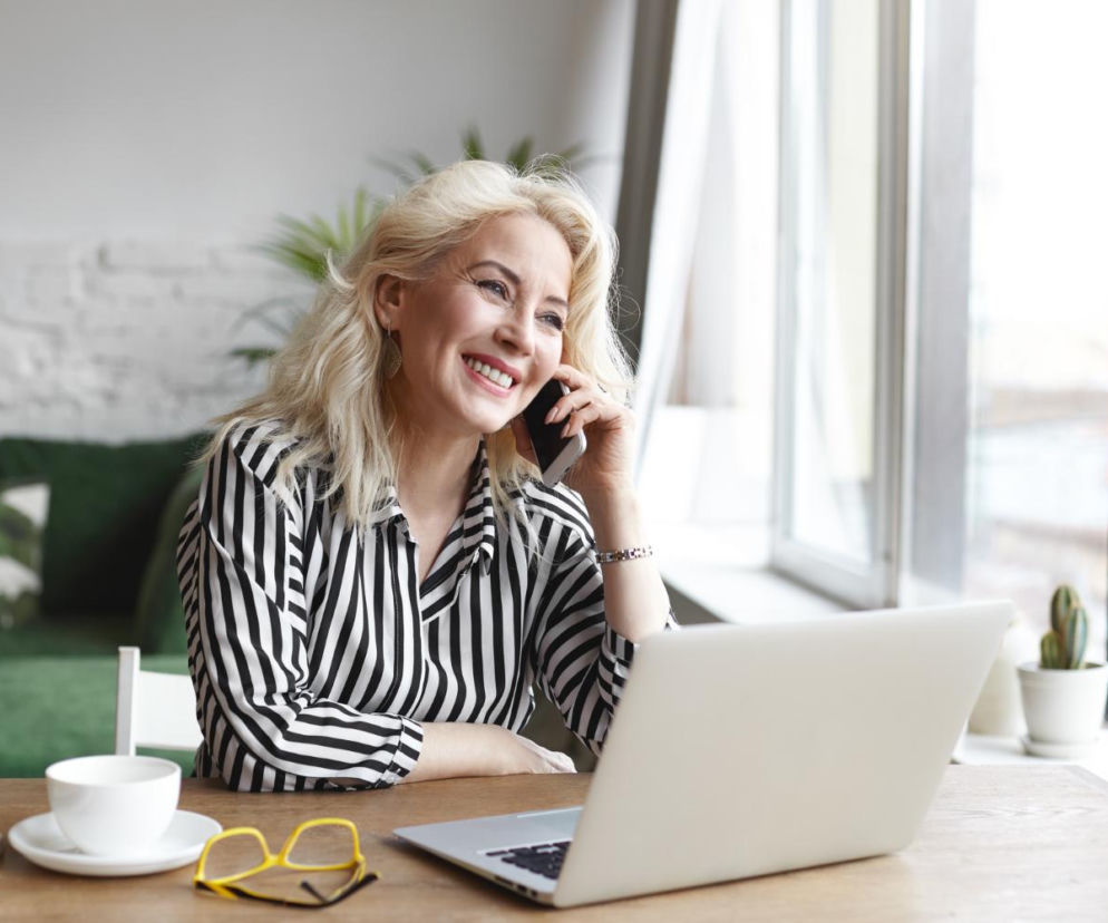 Uśmiechnięta bizneswoman rozmawia przez telefon przy laptopie. O nowej definicji sukcesu Polek przeczytasz na Eska.
