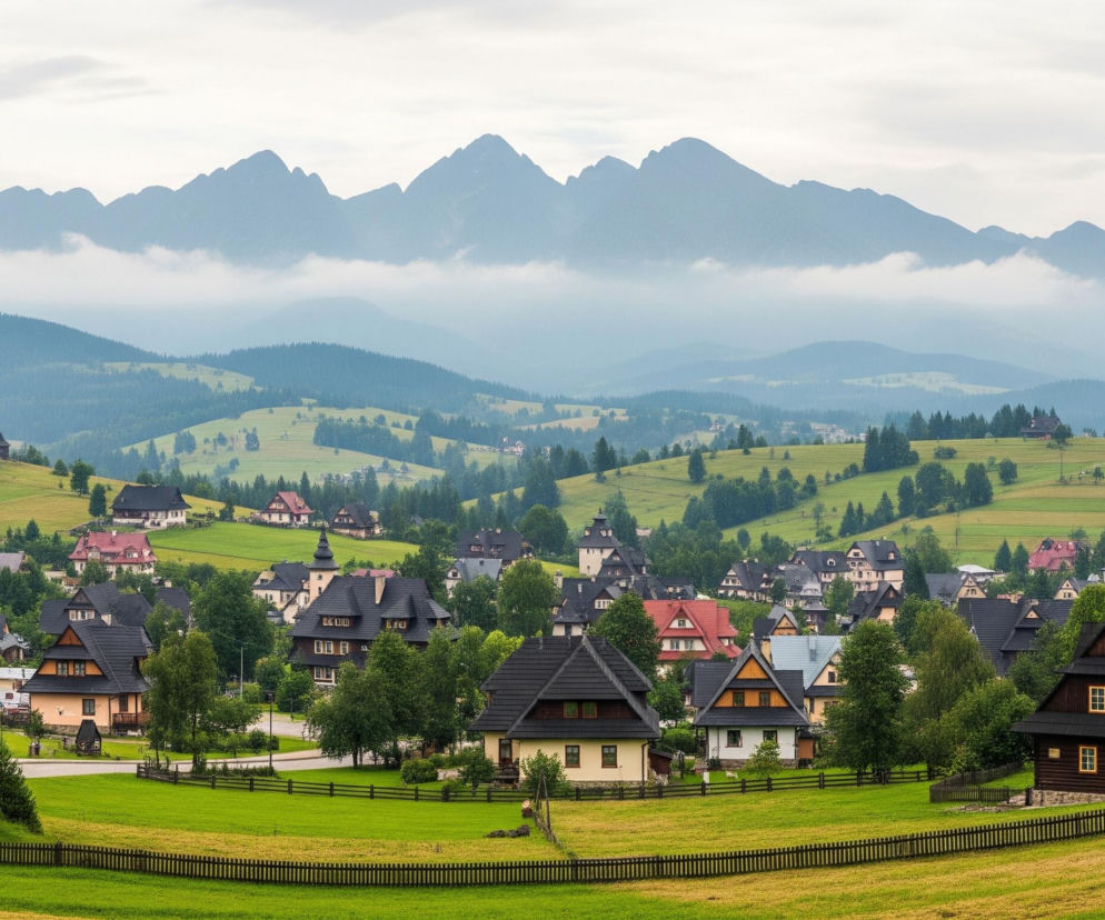 Na pierwszym planie, w dolnej części obrazu, rozciąga się zielone, falujące pole otoczone drewnianym płotem. Za płotem, na łagodnym wzniesieniu, widoczna jest wiejska zabudowa składająca się z licznych domów o tradycyjnej architekturze, z ciemnymi, spadzistymi dachami i drewnianymi elewacjami w odcieniach brązu, beżu i bieli, niektóre z nich ozdobione są pomarańczowymi lub czerwonymi akcentami. Domy są porozrzucane na zielonych wzgórzach, poprzecinanych drogami i otoczone bujną roślinnością, głównie drzewami iglastymi i liściastymi, które nadają krajobrazowi zielony, żywy charakter. W tle dominują majestatyczne, szaro-niebieskie pasma górskie, częściowo przesłonięte przez lekkie mgły lub chmury, które tworzą warstwowe tło pod jasnym, zachmurzonym niebem.