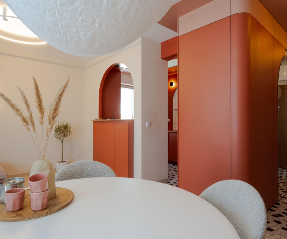 Nowoczesny salon z terakotową zabudową w formie łuków i biały stół z dekoracjami. O tym wnętrzu przeczytasz na Urządzamy.