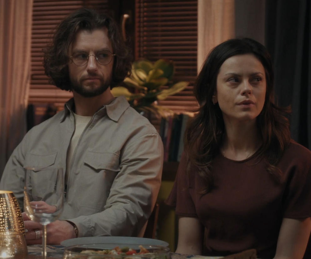 Mariusz (Mateusz Mosiewicz) i Kasia (Paulina Lasota) siedzą przy stole. Mariusz, z brodą i okrągłych okularach, ma na sobie beżową koszulę. Kasia w brązowej bluzce, z długimi włosami, patrzy w prawo. Przed nimi kieliszek i talerz. Więcej informacji o serialu M jak miłość znajdziesz na Super Seriale.